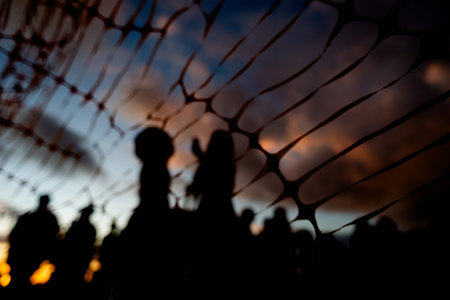 Unidentified people silhouetted through red ribbon fence against dramatic sunset. People on vacation. Travel.の写真素材