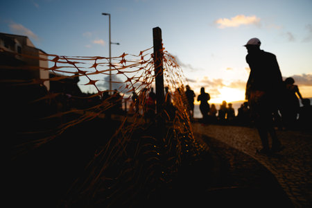 Silhouette of unidentified people next to a ribbon fence against dramatic sunset. People on vacation. Travel.の写真素材