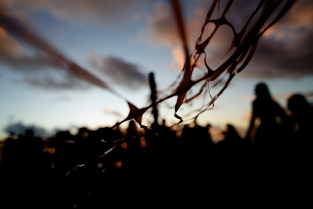 Unidentified people silhouetted through red ribbon fence against dramatic sunset. People on...
