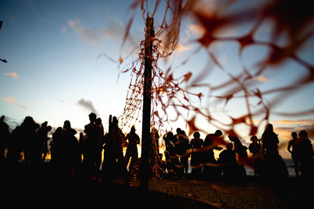 Unidentified people silhouetted through red ribbon fence against dramatic sunset. People on...