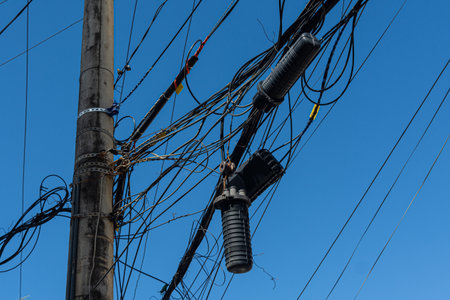 A power pole with a tangle of wires and cables against a blue sky. Industry, structure. Publicの写真素材