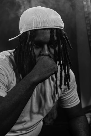 Black and white portrait of a man wearing a hat posing for the camera in a studio against a smoky background. Confident and serious young man.の写真素材