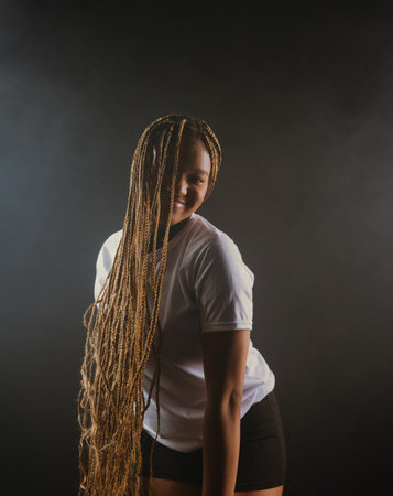 Portrait of a beautiful young woman with braided hair wearing a white outfit and posing for a studio photo. Isolated against a smoky background. Photoshoot.の写真素材