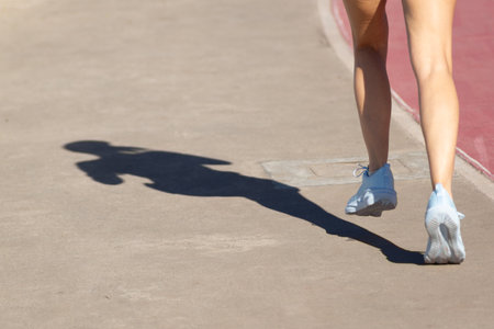 lower part of a person, and their shadow, running along the shore of a beach during strong sunlight. Healthy sports practice.の写真素材