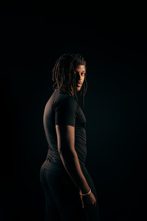 Salvador, Bahia, Brazil - August 30, 2025: Handsome man with dreadlocks wearing black clothing posing for a photo against a black background in a studio.の写真素材