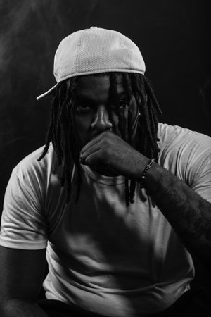 Salvador, Bahia, Brazil - August 30, 2025: Black and white photo of a young Rastafarian man wearing a hat posing for a photo in a studio isolated on a smoky background. Salvador, Brazil.の写真素材