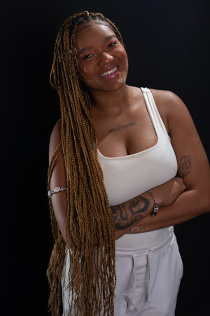 Salvador, Bahia, Brazil - August 30, 2025: beautiful young woman with braided hair, arms crossed, posing for a studio photo against a black background. Salvador, Brazil.の写真素材