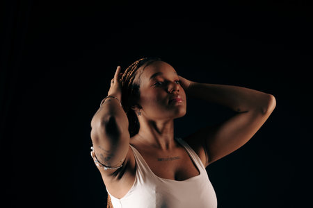 Salvador, Bahia, Brazil - August 30, 2025: Young woman with hands in braided hair posing for a studio photo against a black background. Salvador, Brazil.の写真素材