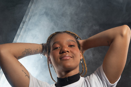 Salvador, Bahia, Brazil - August 30, 2025: Woman with braids posing for a studio photo, holding her hair, isolated against a smoky background. Salvador, Brazil.の写真素材