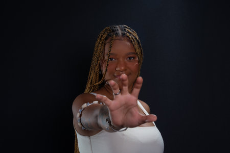 Salvador, Bahia, Brazil - August 30, 2025: Beautiful young woman with braids gesturing to the camera in a studio against a black background. Salvador, Brazil.の写真素材
