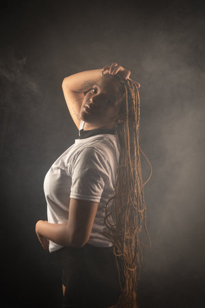 Salvador, Bahia, Brazil - August 30, 2025: Woman with braids posing for a studio photo, holding her hair, isolated against a smoky background. Salvador, Brazil.の写真素材