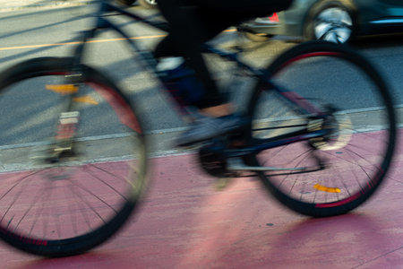 A speeding cyclist is captured in motion blur as he pedals along a reddish-pink bike path on a busy...