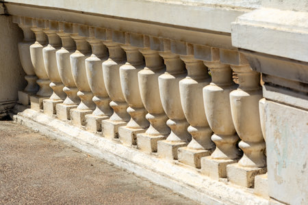 Photograph of an antique balustrade made of light stone or concrete, with symmetrical columns and a classic shape. The image highlights the craftsmanship and the natural wear caused by time.の写真素材