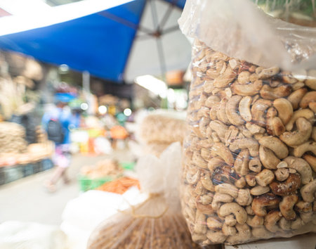A close-up of large plastic bags filled with mixed nuts, including cashews and almonds, stacked on a shelf.の写真素材