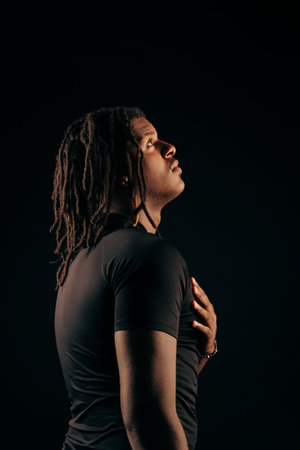 Man with dreadlocks wearing a black shirt looking up in a studio. Isolated on a black background. Photo model.の写真素材