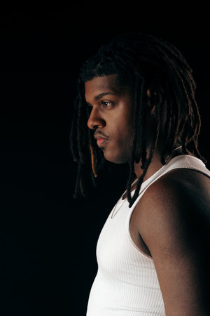 Handsome man with dreadlocks wearing a white shirt looking to the side. Isolated on a black studio...