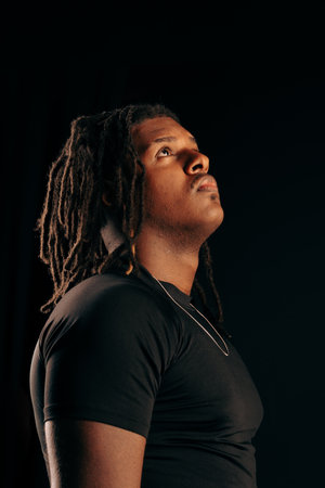 Handsome man with dreadlocks wearing a black shirt looking at the camera in a studio. Isolated on a...