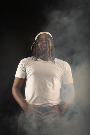 Handsome young man with dreadlocks and a white hat posing for the camera during a studio photoshoot....