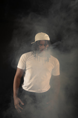 Handsome young man with dreadlocks and a white hat posing for the camera during a studio photoshoot....