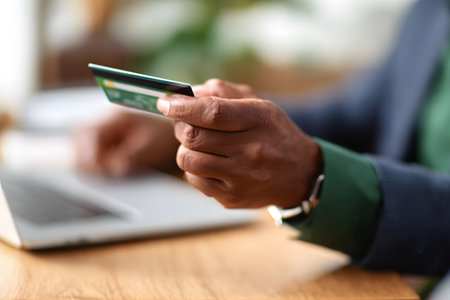 Close-up of a man's hands holding a credit card, about to finalize an online purchase on a laptop, taking advantage of Black Friday promotions. Focus on digital payment, e-commerce, and seasonal sales.の素材