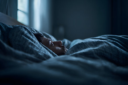 Dark and atmospheric close-up of the face of a person sleeping deeply. The face is partially hidden under a navy blue or dark gray blanket.の素材