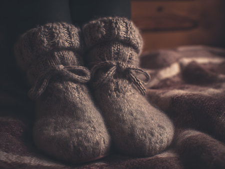 Close-up of a pair of soft, gray knitted woolen socks with bows, over a brown, checkered blanket or throw, conveying a feeling of warmth, comfort, and winter coziness.の素材