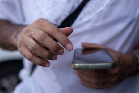 Close-up of a person's hands holding and interacting with a dark-screen smartphone. The person is wearing a white shirt.の写真素材