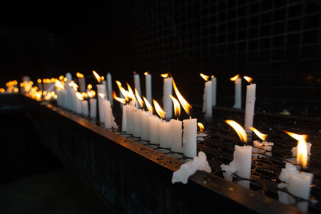 Close-up of several white candles lit in a dark votive candle holder, symbolizing requests and...