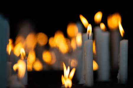 Close-up of several white candles lit in a dark votive candle holder, symbolizing requests and gratitude in a religious setting.の写真素材