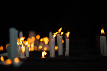 Close-up of several white candles lit in a dark votive candle holder, symbolizing requests and...