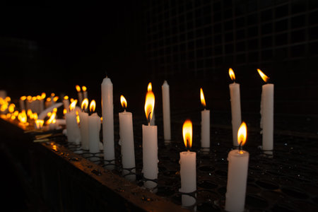 Close-up of several white candles lit in a dark votive candle holder, symbolizing requests and...