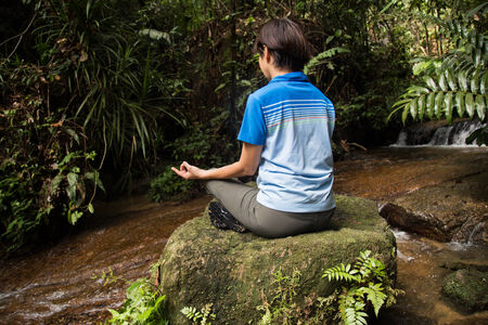 Women meditating in the woods next to a streamの写真素材