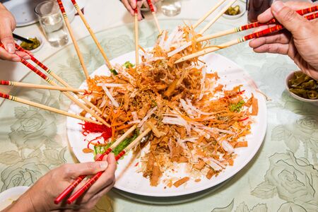 A group of people mixing and tossing Yee Sang dish with chop sticks. Yee Sang is a popular delicacy taken during Chinese New Year, believed to bring good fortune and luckの写真素材