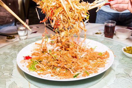 A group of people mixing and tossing Yee Sang dish with chop sticks. Yee Sang is a popular delicacy taken during Chinese New Year, believed to bring good fortune and luckの写真素材