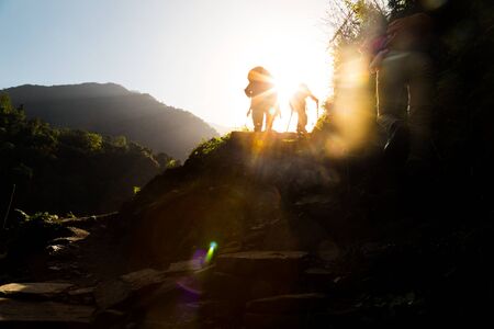 Three people in silhouette hiking at highland towards sunrise.  Lens flare intended.の写真素材