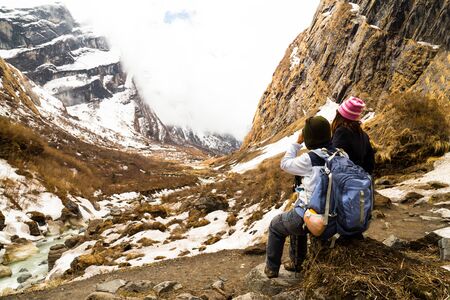 Two female hikers resting while enjoying the serene view of the snowy trekの写真素材