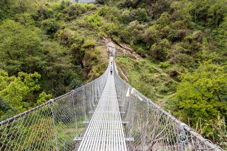 Hikers crossing a long metal suspension bridgeの写真素材