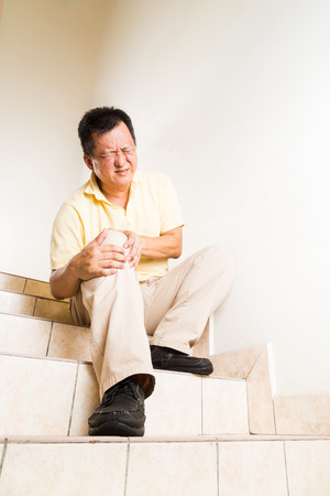 Matured man suffering acute knee joint pain seated on staircaseの写真素材