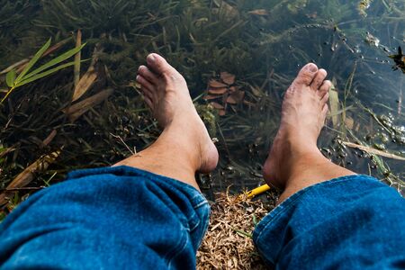 Legs and feet relaxing in front of serene fresh water pondの写真素材