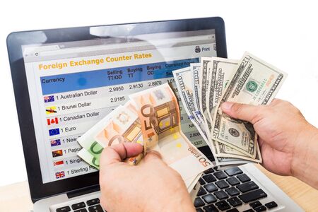 Hand sorting USD and EURO in front of currency exchange chart on computer screen.の写真素材