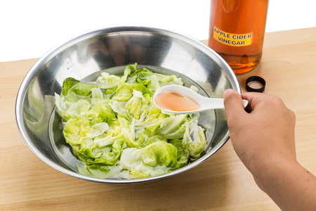 Hand pouring spoonful of Apple Cider Vinegar to soak and remove pesticides residue from vegetableの写真素材