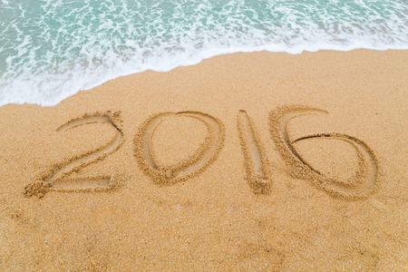 2016 inscription written on sandy beach with wave approaching.
