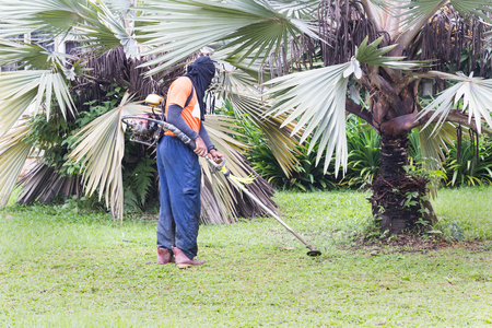 Worker with protective clothing cutting grass with grass cutter machine at residential area