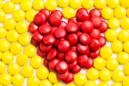 Heart shape with red milk chocolate candies against yellow chocolate candies backgroundの写真素材