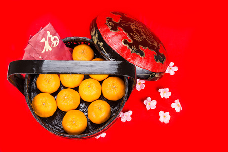 Juicy mandarin oranges in traditional basket with Good Luck Chinese character on red packets in red backgroundの写真素材