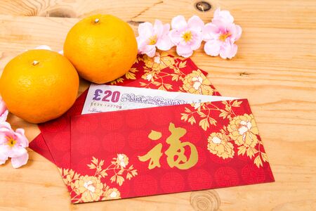 Hung Bao or red packet with Good Fortune Chinese character filled with Sterling Pound currency, displayed with mandarin orangesの写真素材