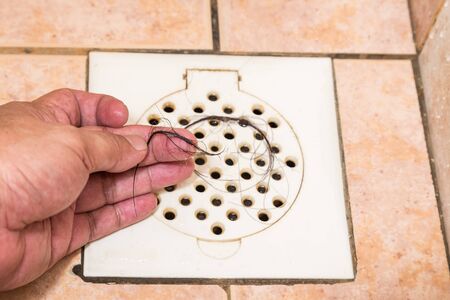 Hand inspecting bunch of hair trapped at bathroom shower drain trap outletの写真素材