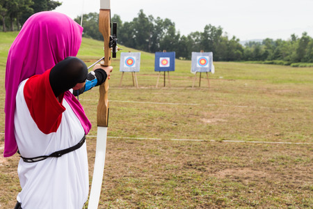 Person practicing at outdoor archery target range, aiming at target board