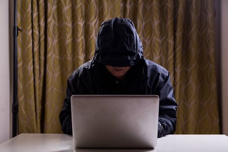 Asian hacker hacking computer network with laptop in dark