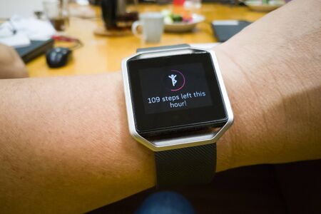 Perspective view of person reading wrist watch with heart and steps tracker in office workingの写真素材